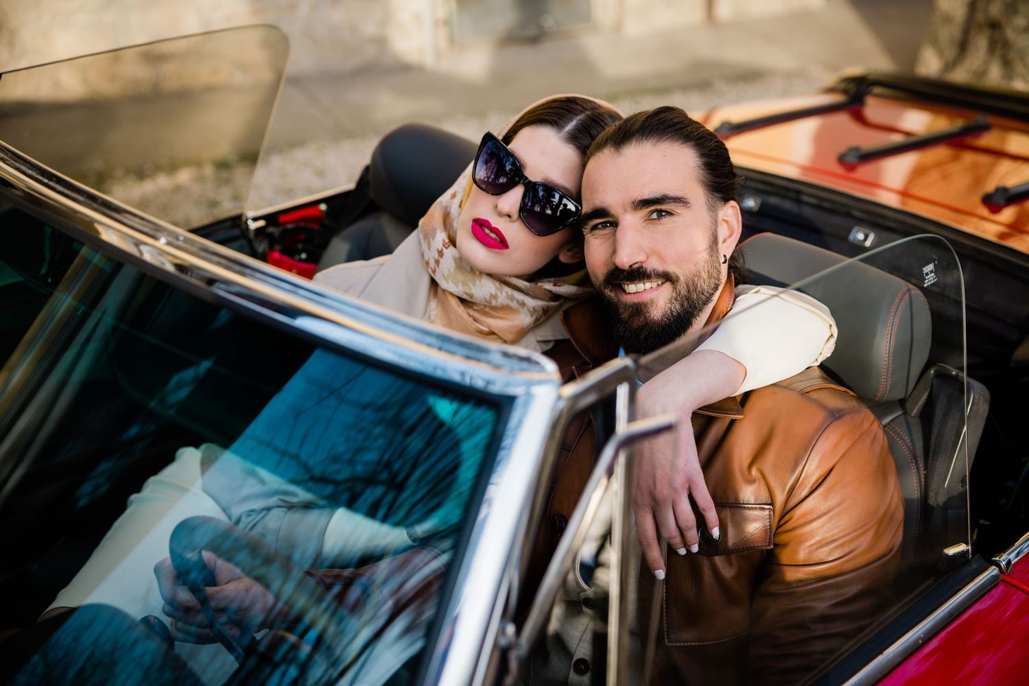 A couple sitting together in a vintage convertible car during a stylish photoshoot.