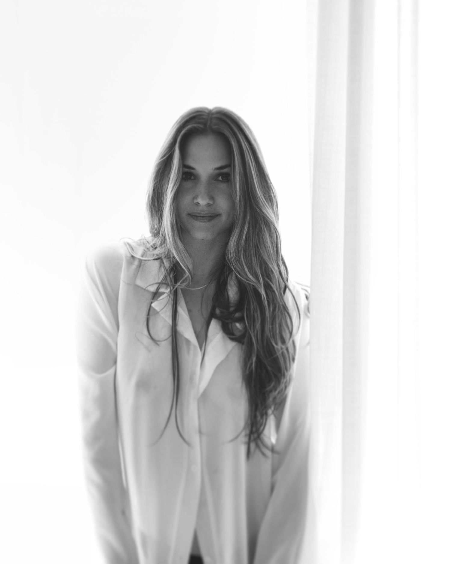 Soft black and white portrait of a woman near window in relaxed pose