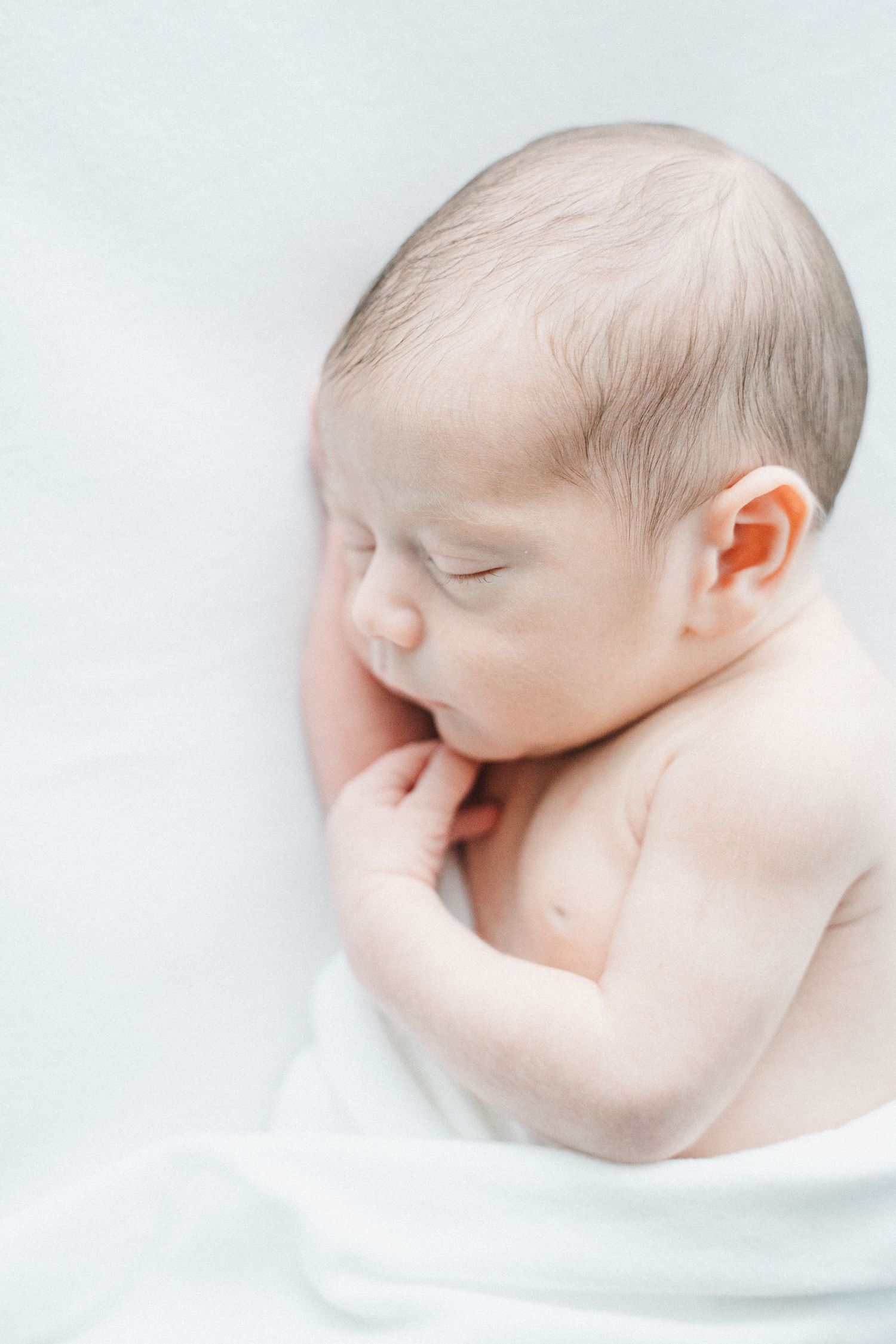 Soft newborn portrait with white swaddle and blue eyes open