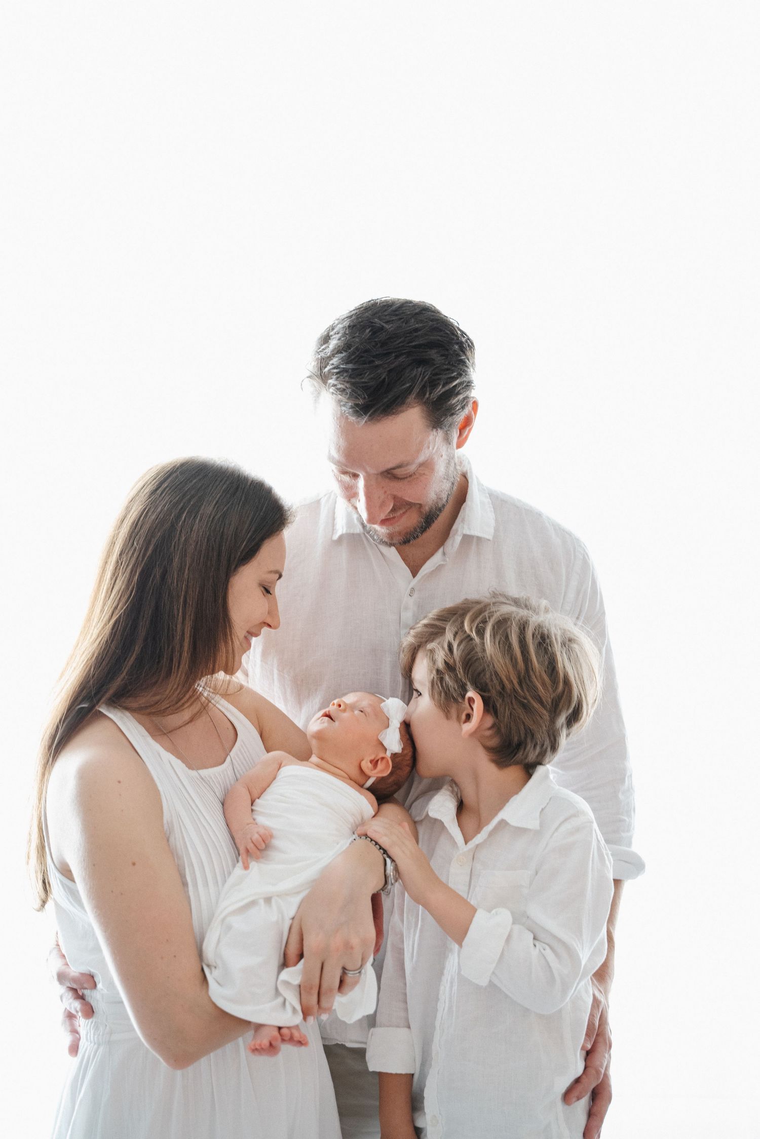 Family with young kids smiling while holding newborn at home