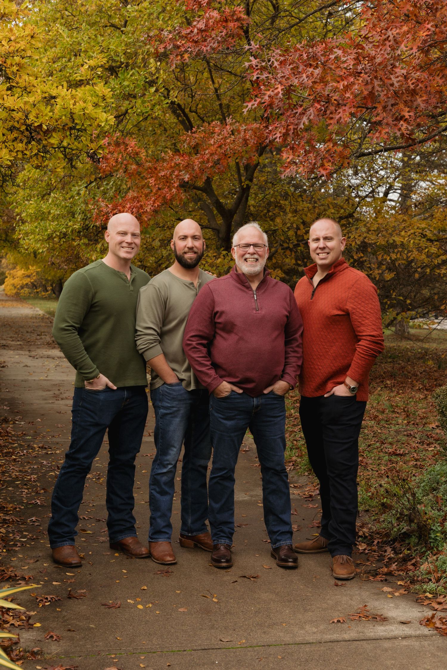 Four men posing outdoors on a path surrounded by vibrant autumn foliage in fall colors.