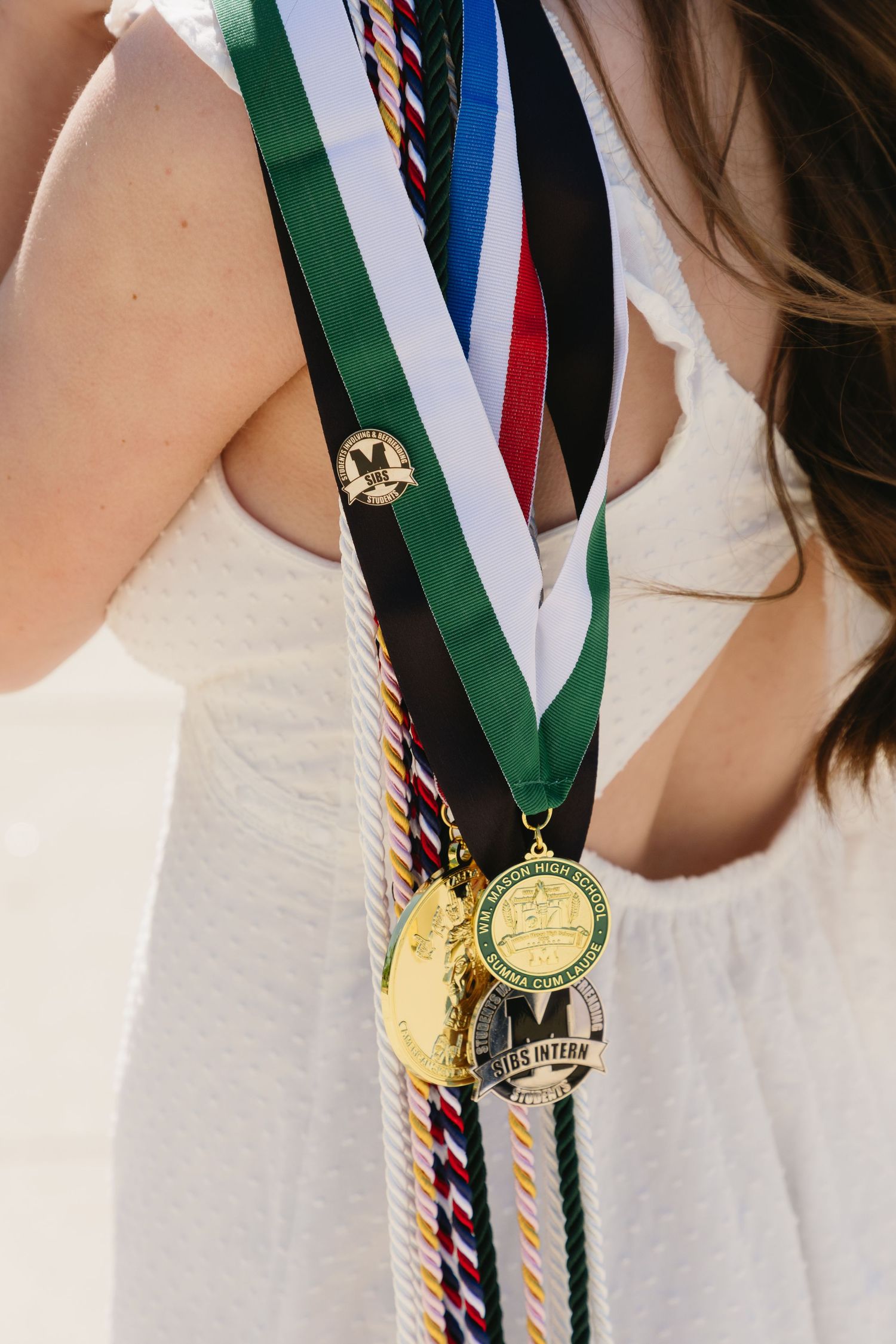 Close-up of graduation medals on colorful ribbons worn by a student in a white dress.