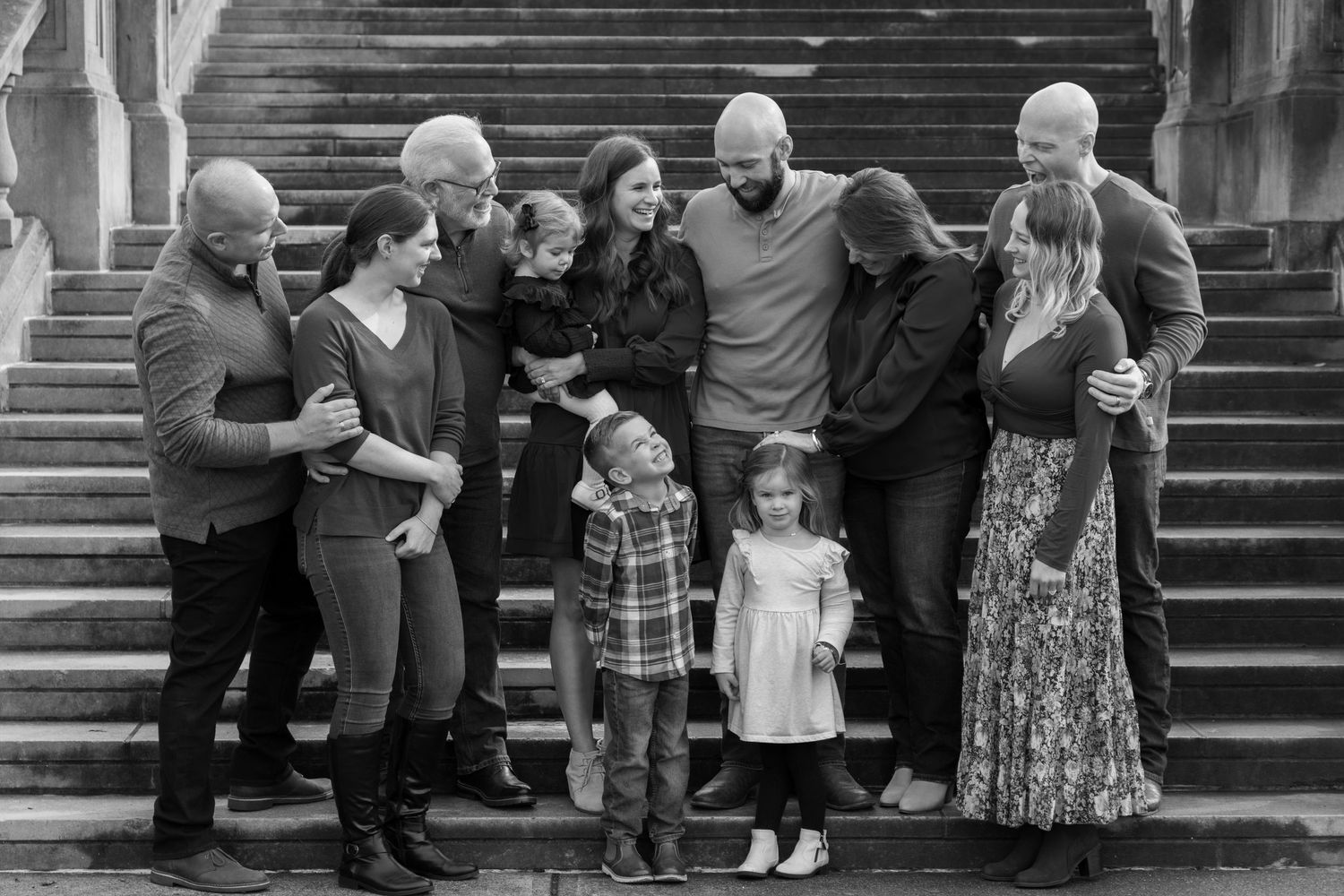Black and white family portrait on stone steps with adults and two young children laughing together.