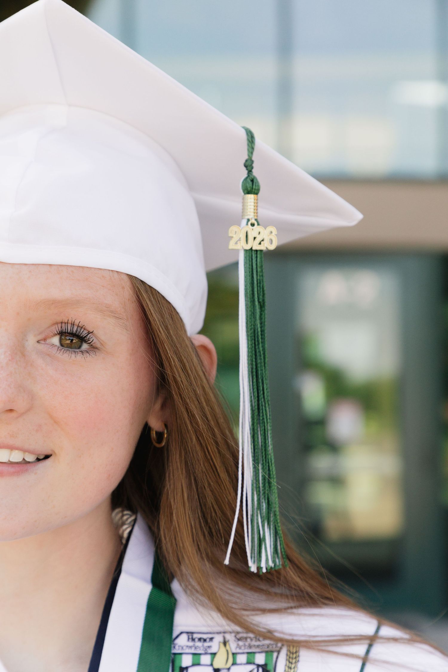 Young woman in white graduation cap with green and white 2020 tassel smiling at her graduation ceremony.