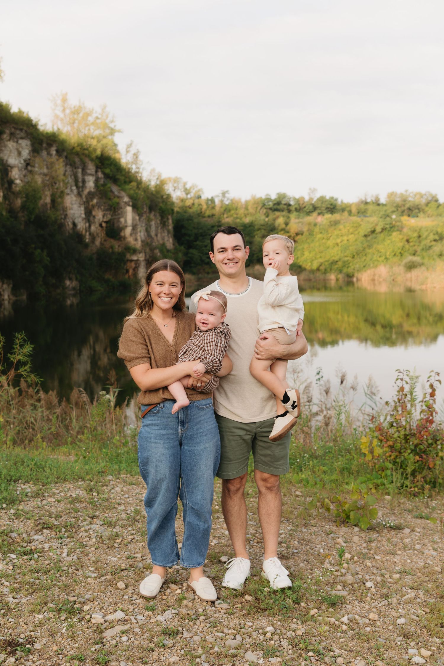 Happy family of four posing by a scenic quarry lake surrounded by lush greenery on a cloudy day.