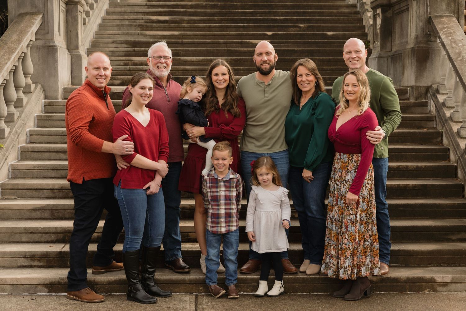 Large family group portrait on stone steps, smiling adults and children in coordinated fall outfits.