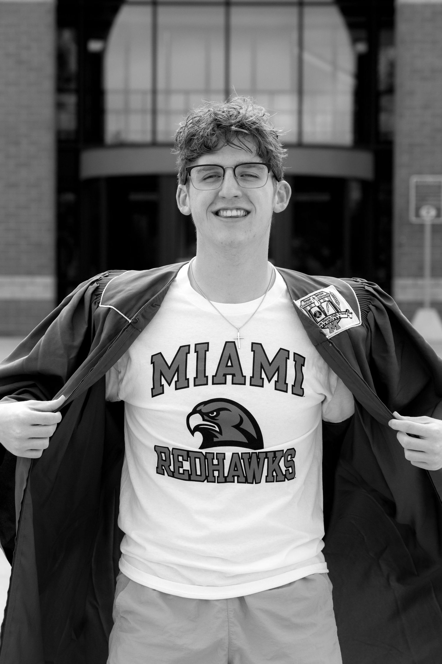 Young man smiling in a Miami Redhawks t-shirt, proudly opening his jacket in a black and white photo.