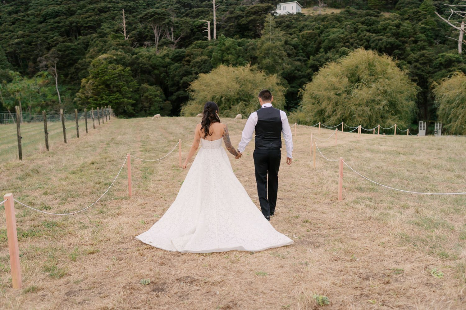 Bride and groom walking hand in hand through a scenic green field on their wedding day.