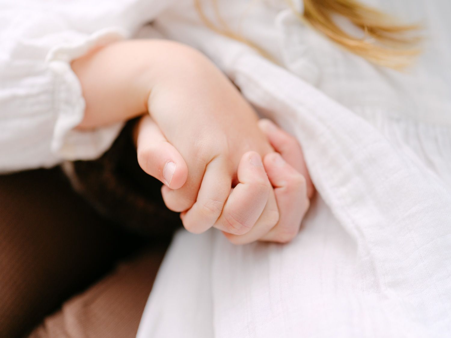 A tender close-up of a baby's small hand gently clasping an adult's finger, wrapped in soft white fabric.