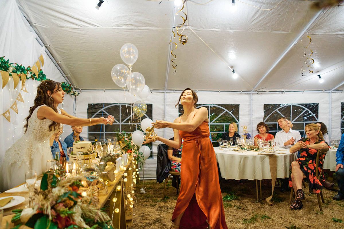 Bridesmaid in orange dress releases balloons at wedding reception inside decorated tent.