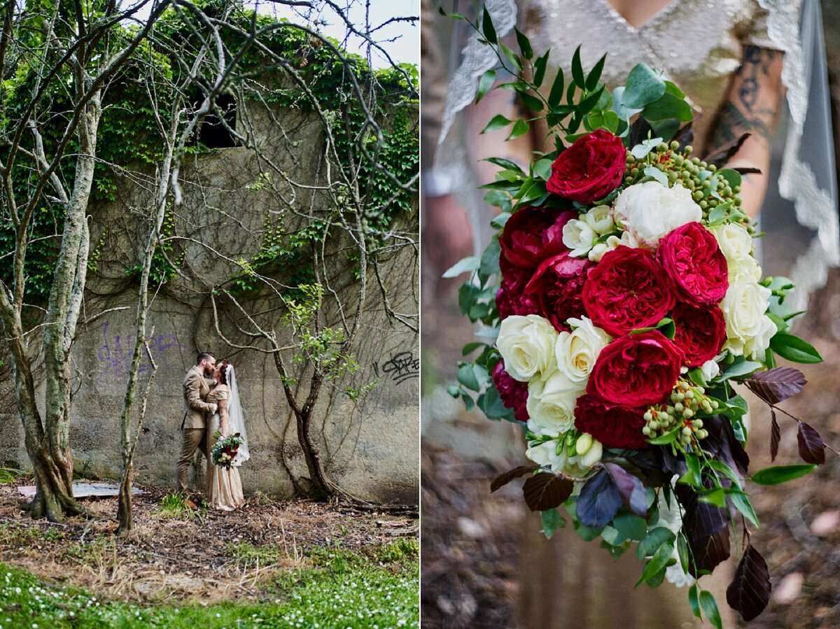 Romantic wedding couple embracing under bare trees beside stone wall, paired with lush red and white bridal bouquet.