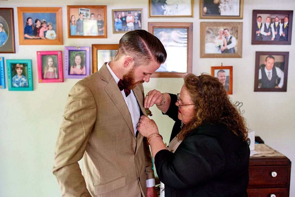 A woman pins a boutonniere on a suited man in a room decorated with framed family photos.