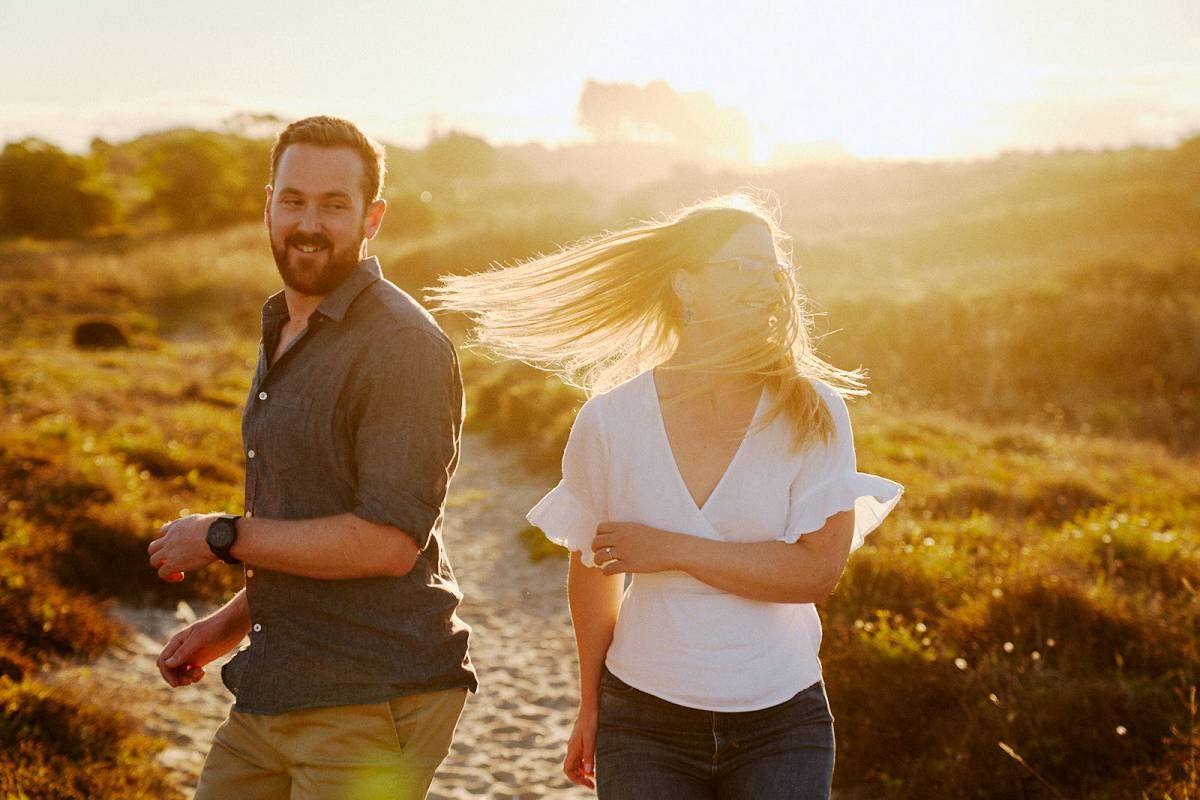 Couple walking on a sunlit trail at golden hour, woman's hair blowing in the wind.