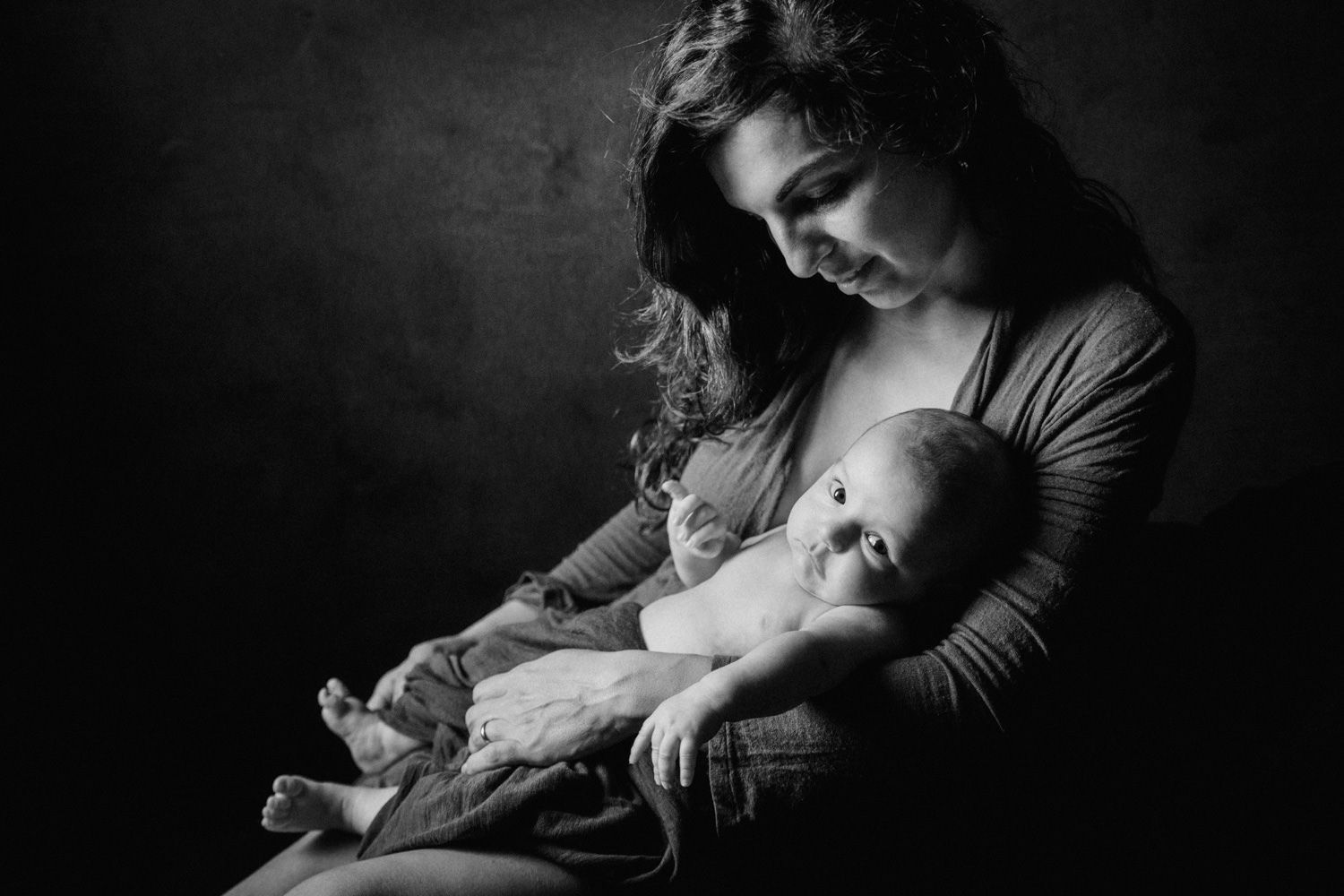 Black and white portrait of a mother tenderly cradling her newborn baby in her arms.