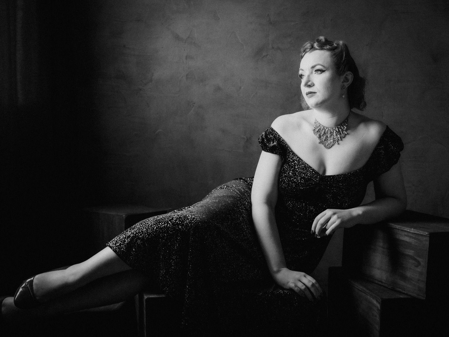 Elegant woman in black lace dress poses gracefully in black and white portrait photography.