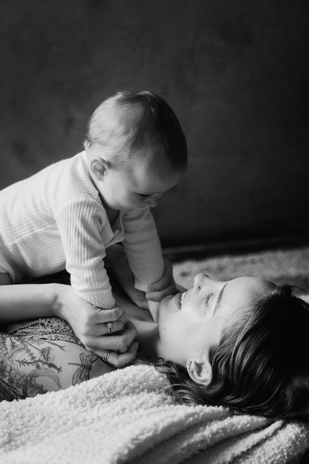 Black and white photo of a mother lying down, lovingly holding her smiling baby up above her face.