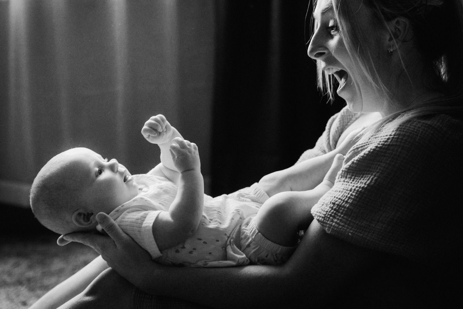Black and white photo of a smiling mother holding her happy baby who raises a tiny fist in a tender moment.