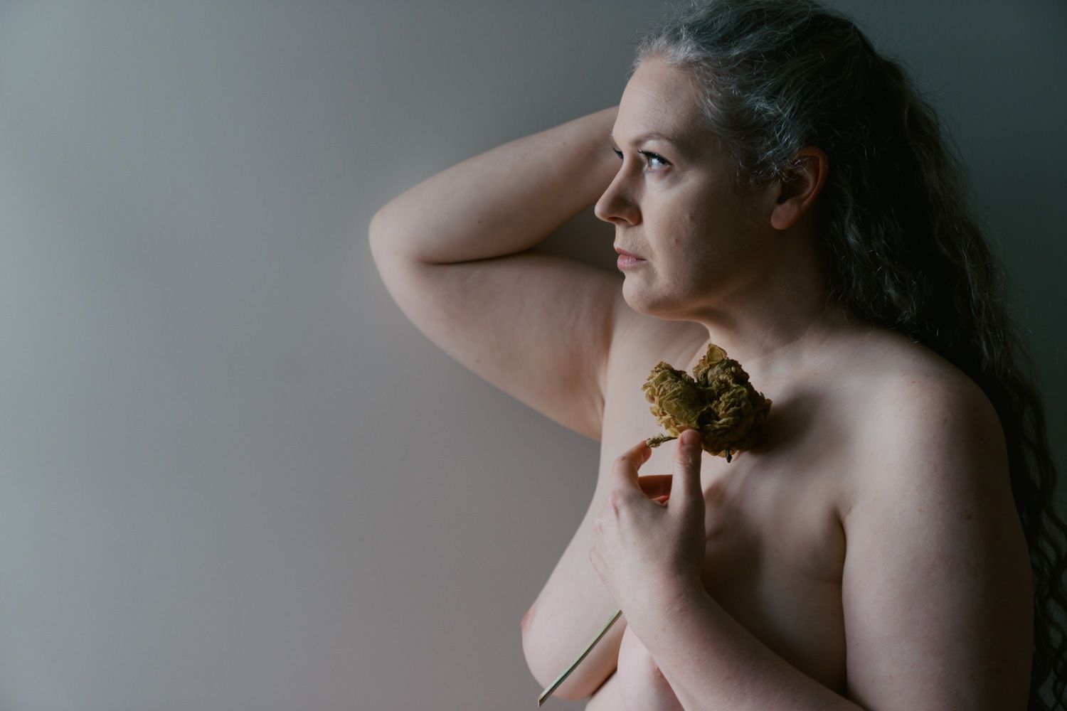 Woman holding a dried flower, posing in a soft-lit boudoir portrait session.