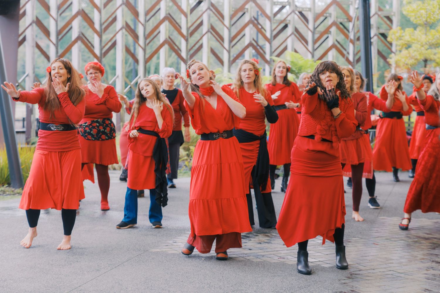 Large group of women in red dresses performing a synchronized dance outdoors at a public event.