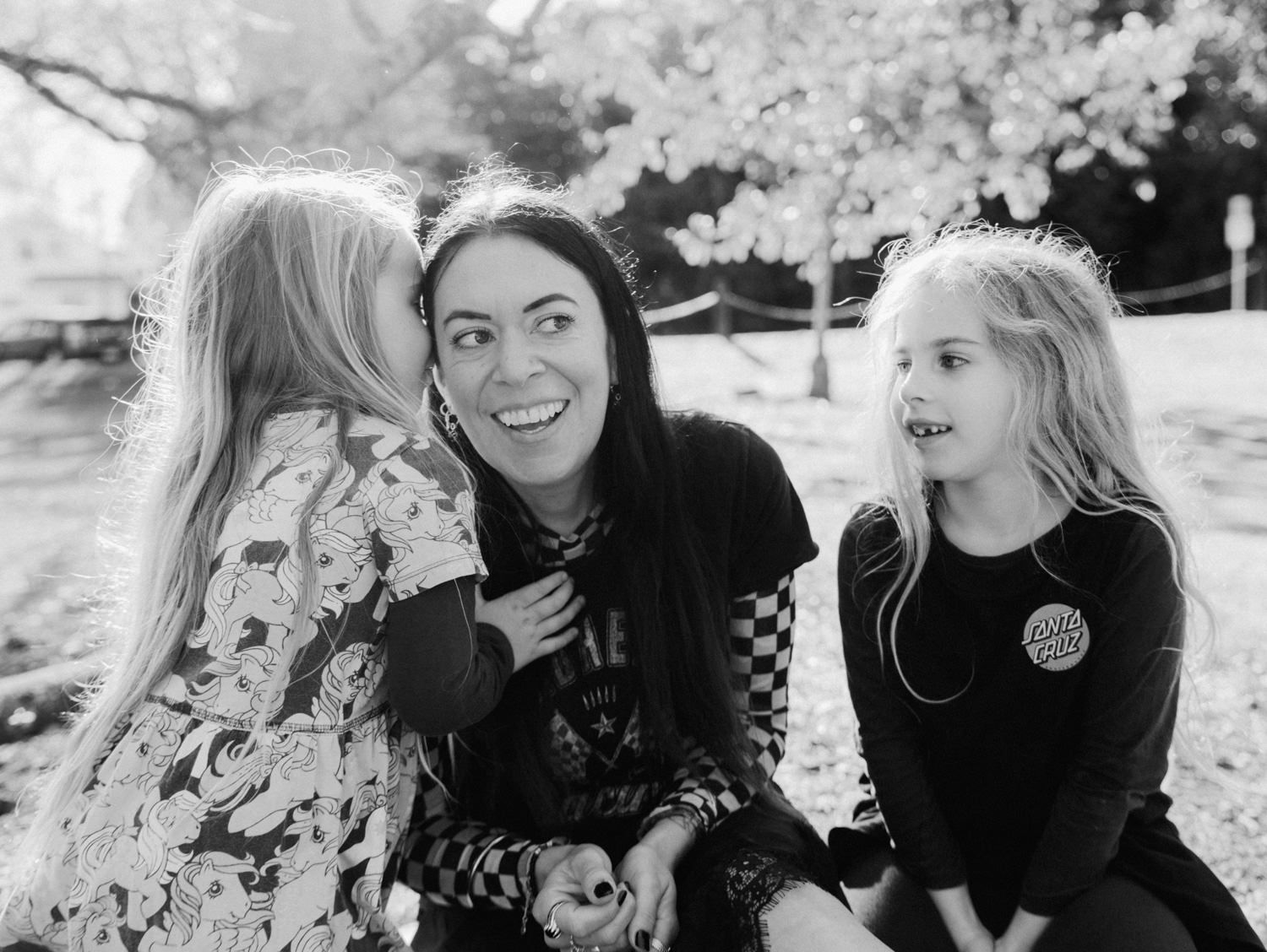 Black and white photo of two girls and a laughing woman sitting together outdoors in a park.