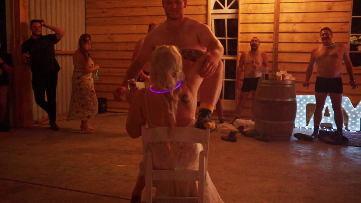 Adults and children dancing at a rustic barn wedding reception with warm lighting and decorative signage.