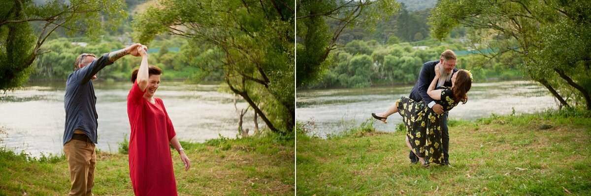 Couple dancing and embracing outdoors near a river with lush green trees during an engagement photo session.