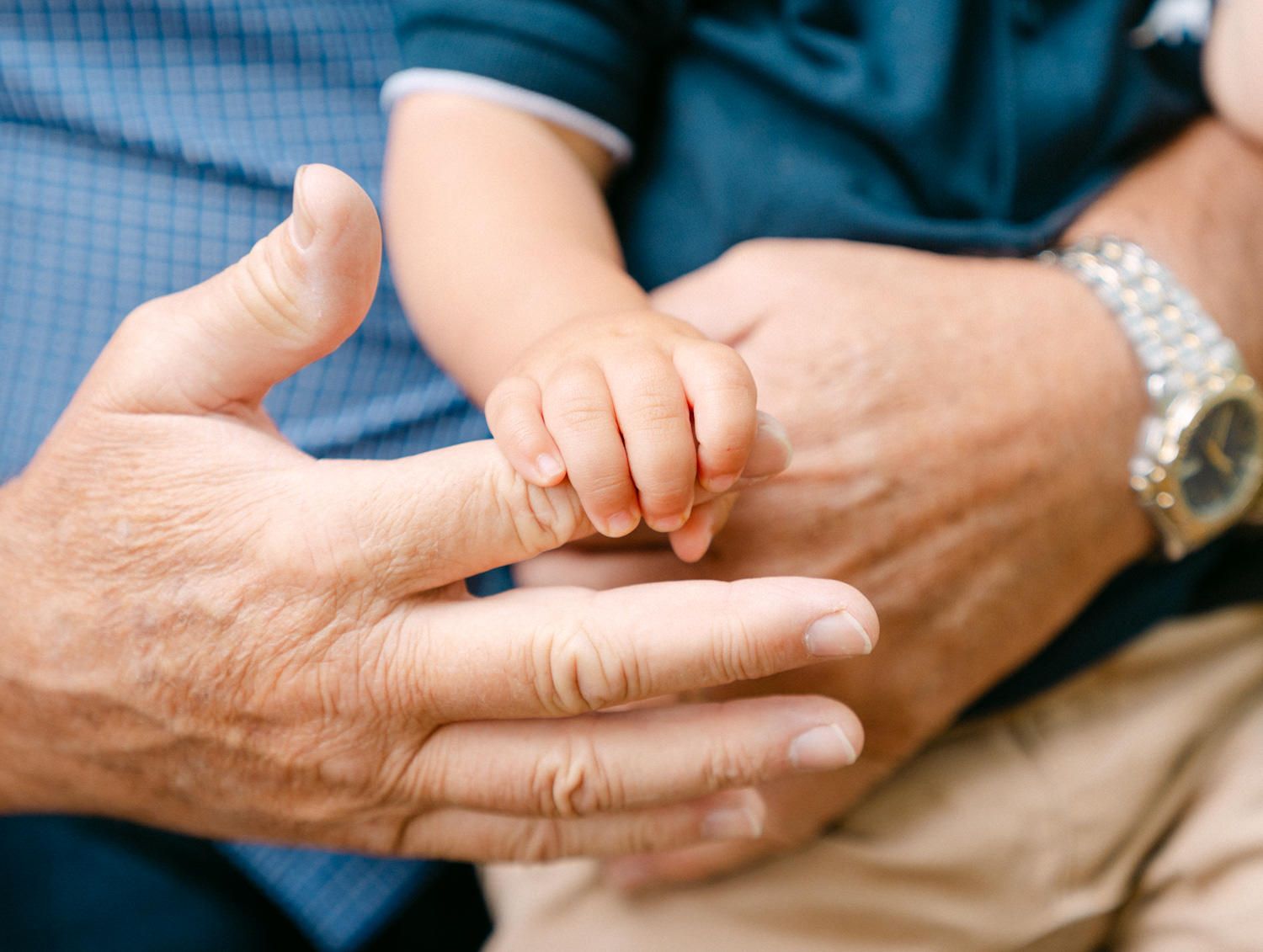 Close-up of a baby's tiny hand grasping an adult's finger, symbolizing family love and generational bond.