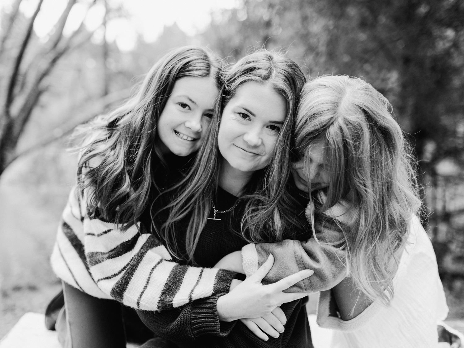 Three young women hugging and smiling together outdoors in a black and white portrait photo.