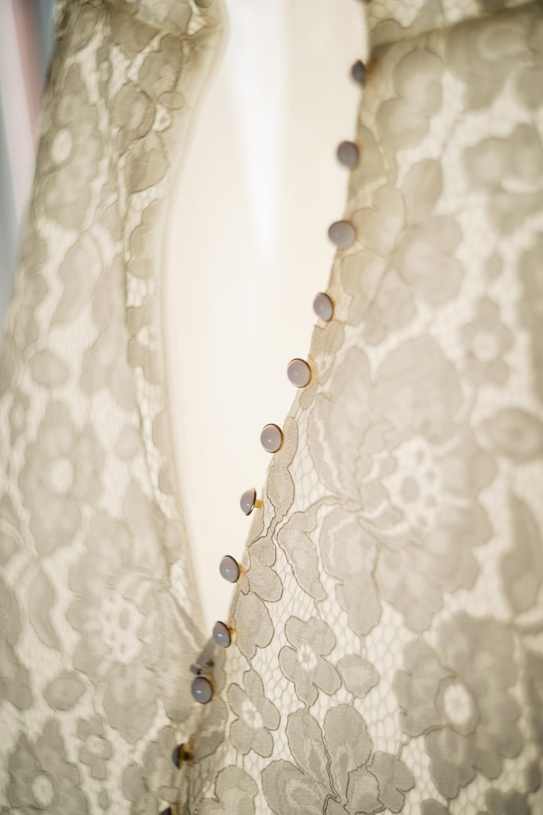 Close-up of an elegant lace wedding dress with delicate floral pattern and small buttons along the back closure.
