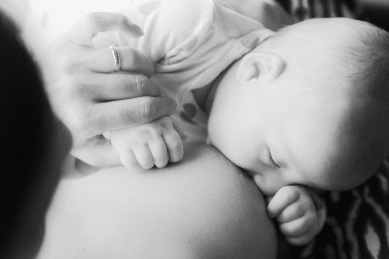 Black and white photo of a sleeping newborn baby cradled in a parent's arms, showcasing a tender bonding moment.