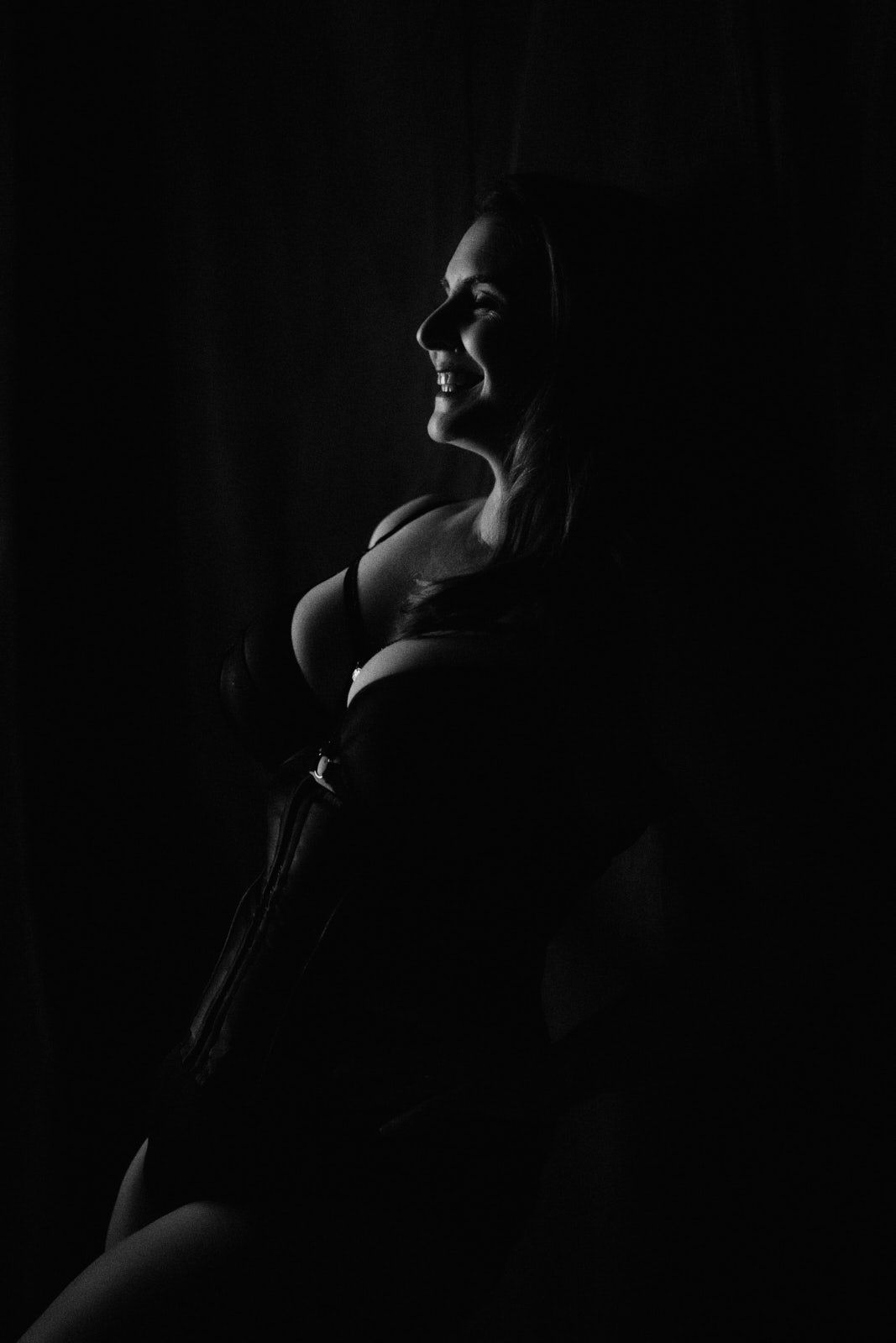 Black and white silhouette portrait of a smiling pregnant woman cradling her baby bump in dramatic low-key lighting.