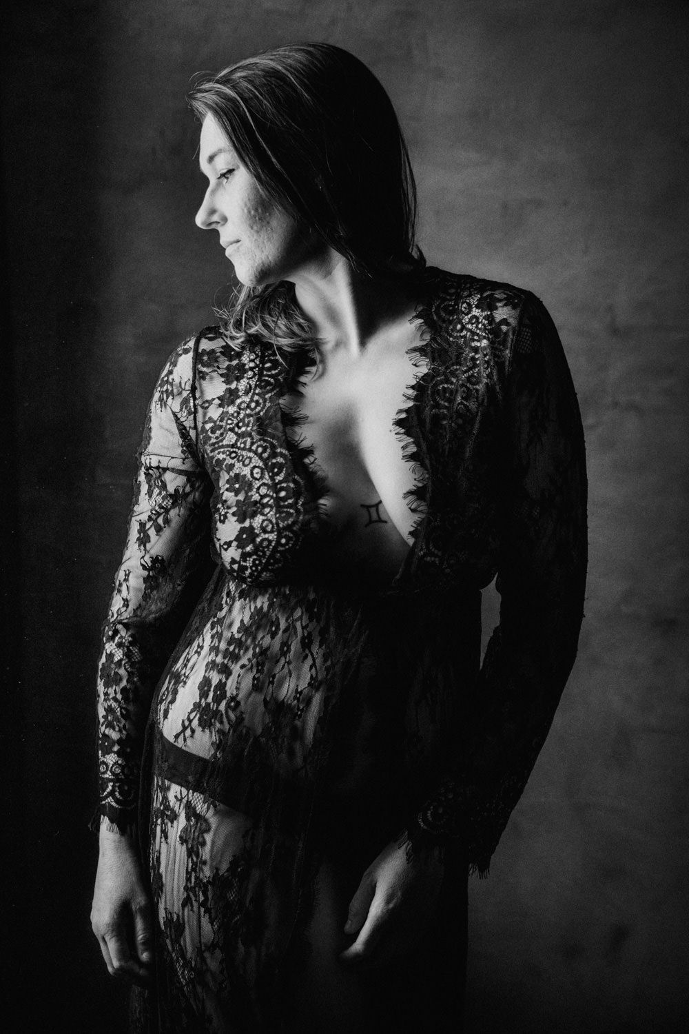 Black and white portrait of a woman in elegant lace dress, looking sideways in dramatic studio lighting.