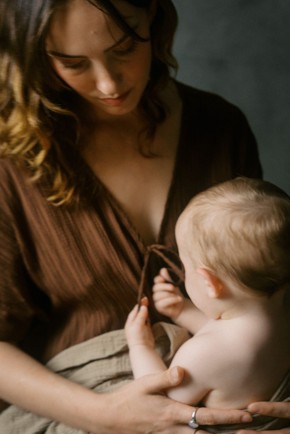 A smiling mother in a brown dress tenderly holds her infant baby, sharing a peaceful bonding moment.