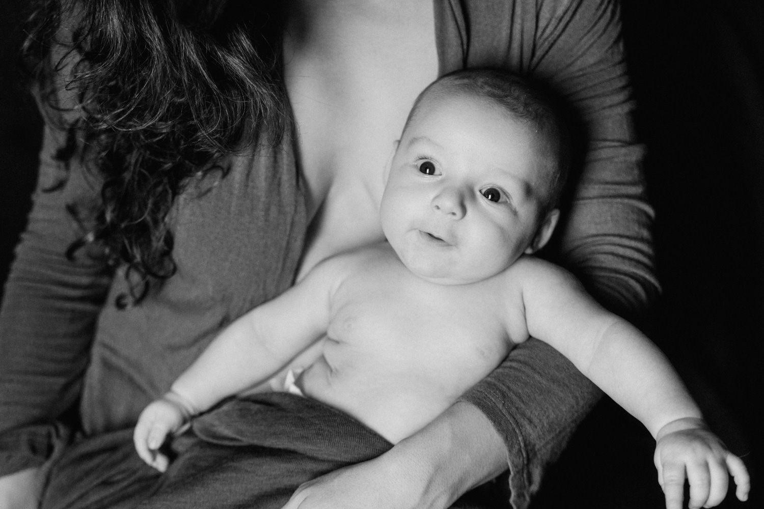 Black and white photo of a newborn baby resting in mothers arms, looking up curiously.