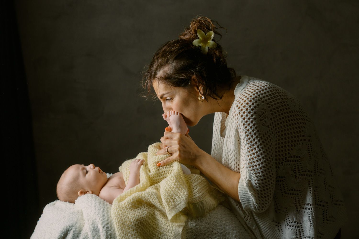 A mother lovingly kisses her newborn baby wrapped in a soft yellow blanket.