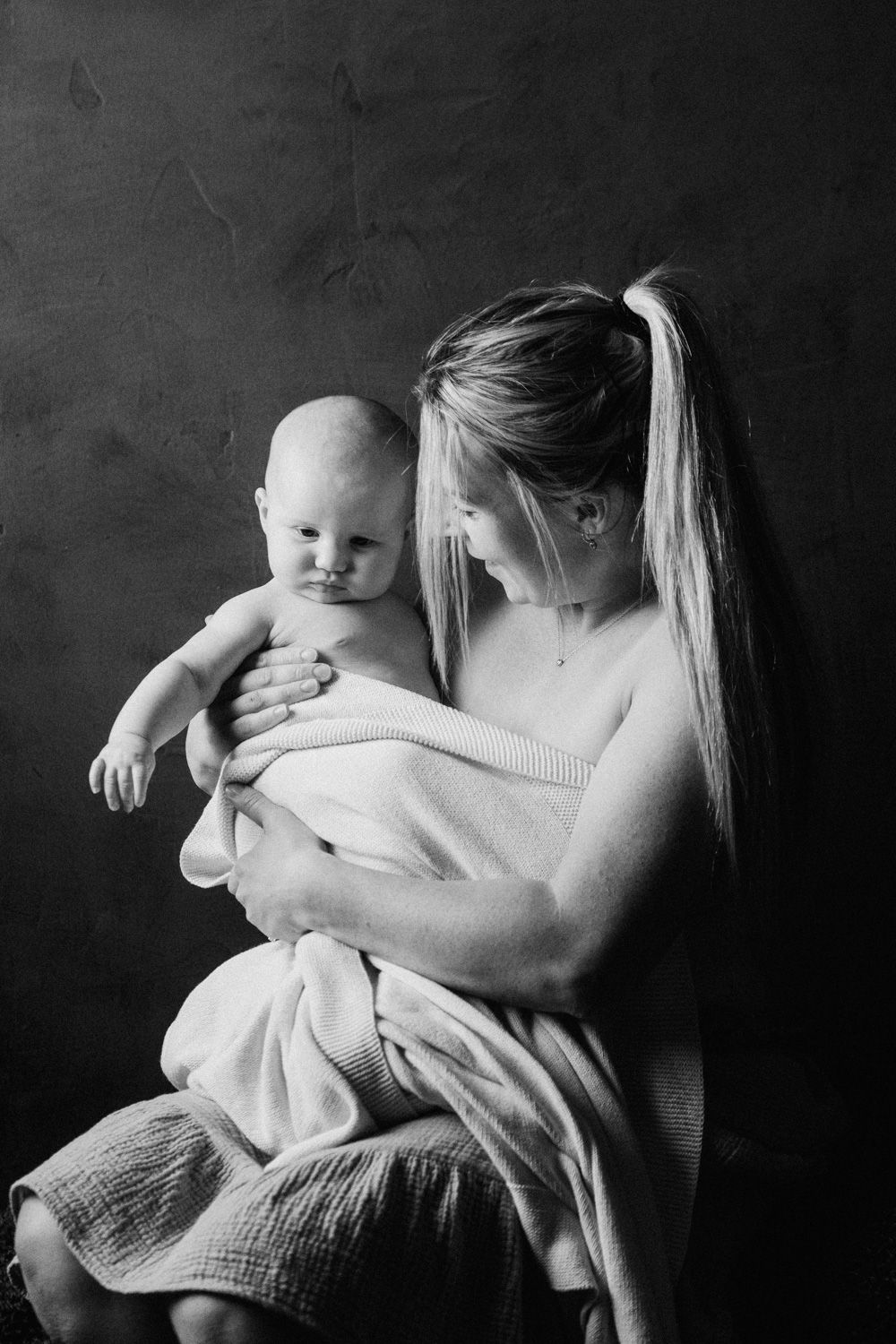 Black and white photo of a mother tenderly holding her newborn baby wrapped in a soft white blanket.