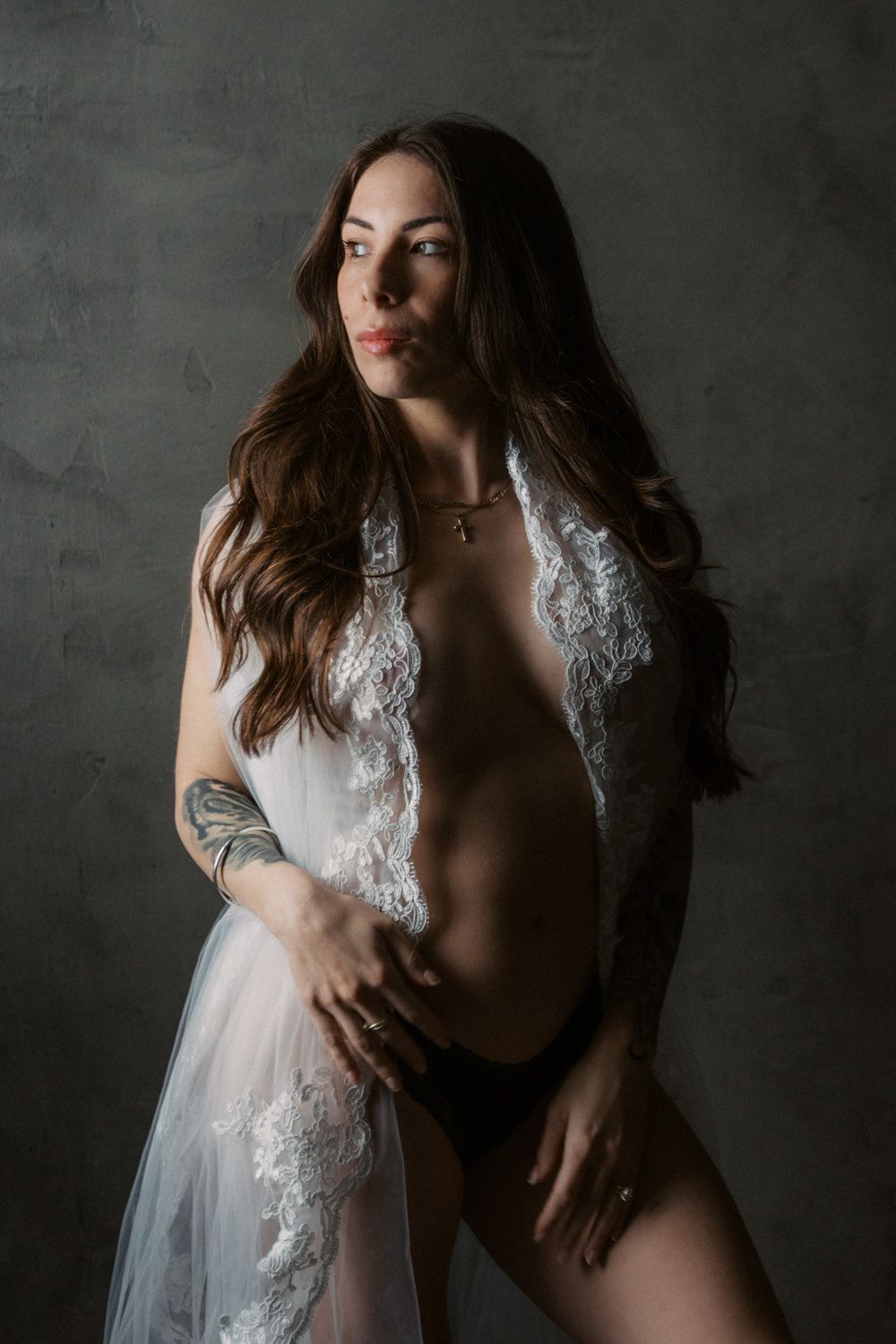Woman in sheer lace robe and black underwear posing confidently against a dark studio background.