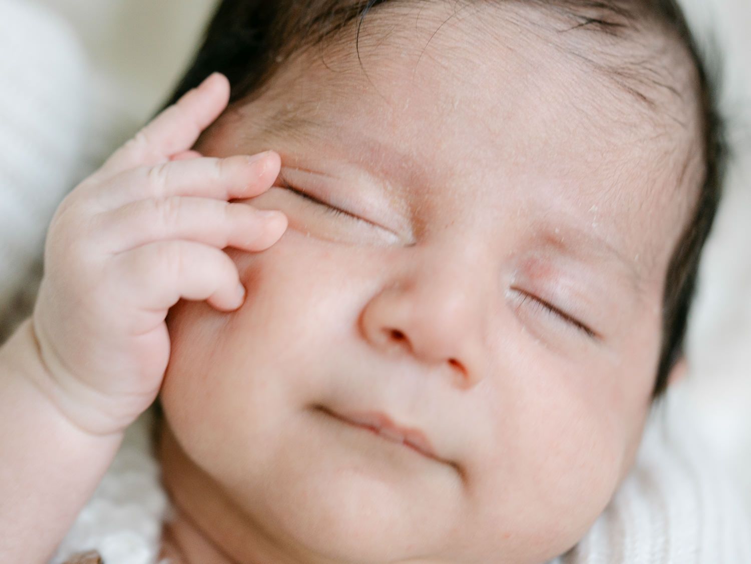 Close-up of a peaceful newborn baby rubbing their eye with a tiny hand while sleeping.