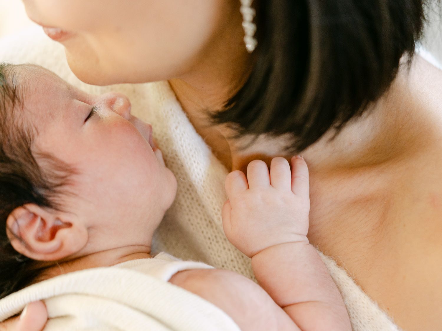 Mother tenderly kissing her sleeping newborn baby held against her chest.