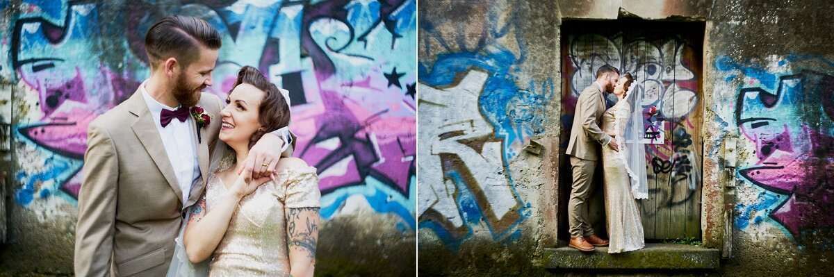 Bride and groom posing romantically in front of vibrant colorful graffiti wall at urban wedding photo shoot.