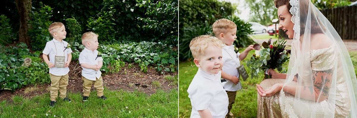 Two young boys in white shirts and khaki pants stand in a garden, while a bride in a veil receives flowers nearby.