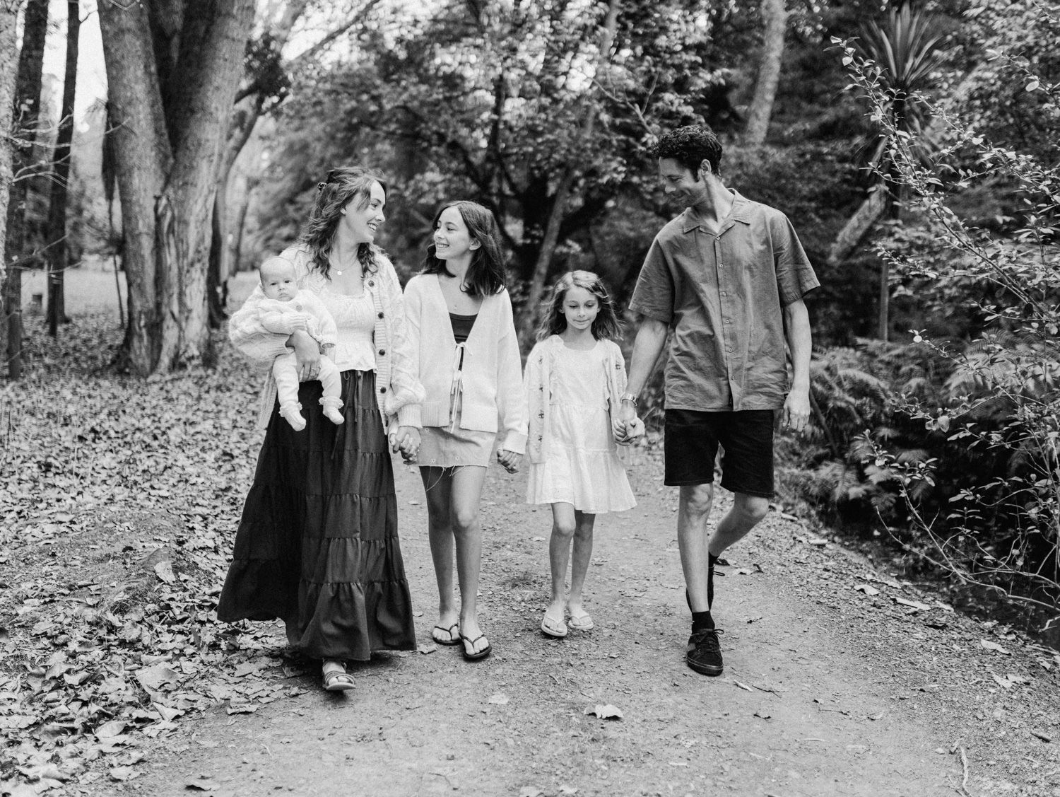Black and white family photo of five people walking together on a tree-lined path outdoors.