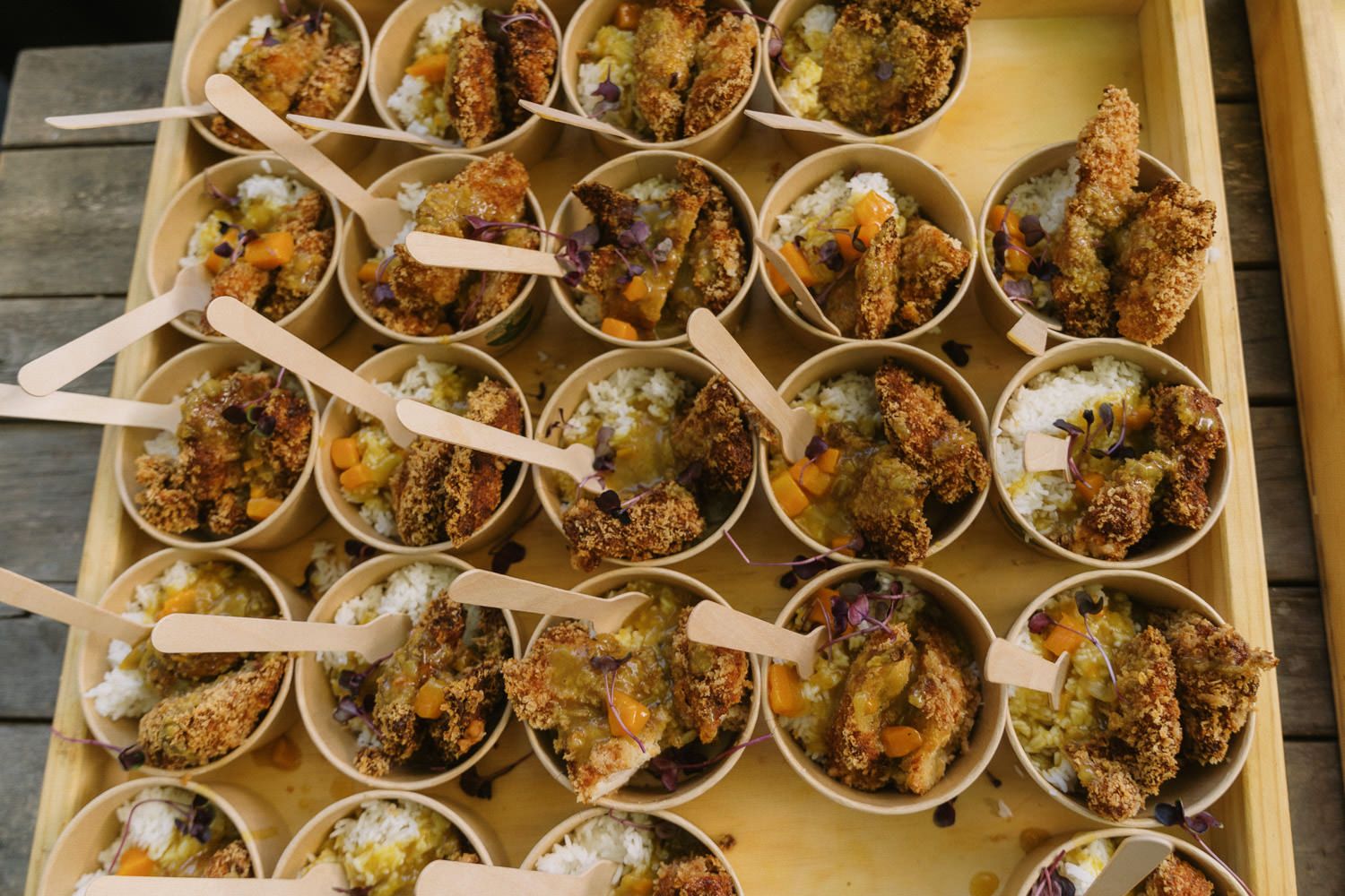 Tray of small cups filled with granola parfaits, each served with a wooden spoon at an outdoor event.