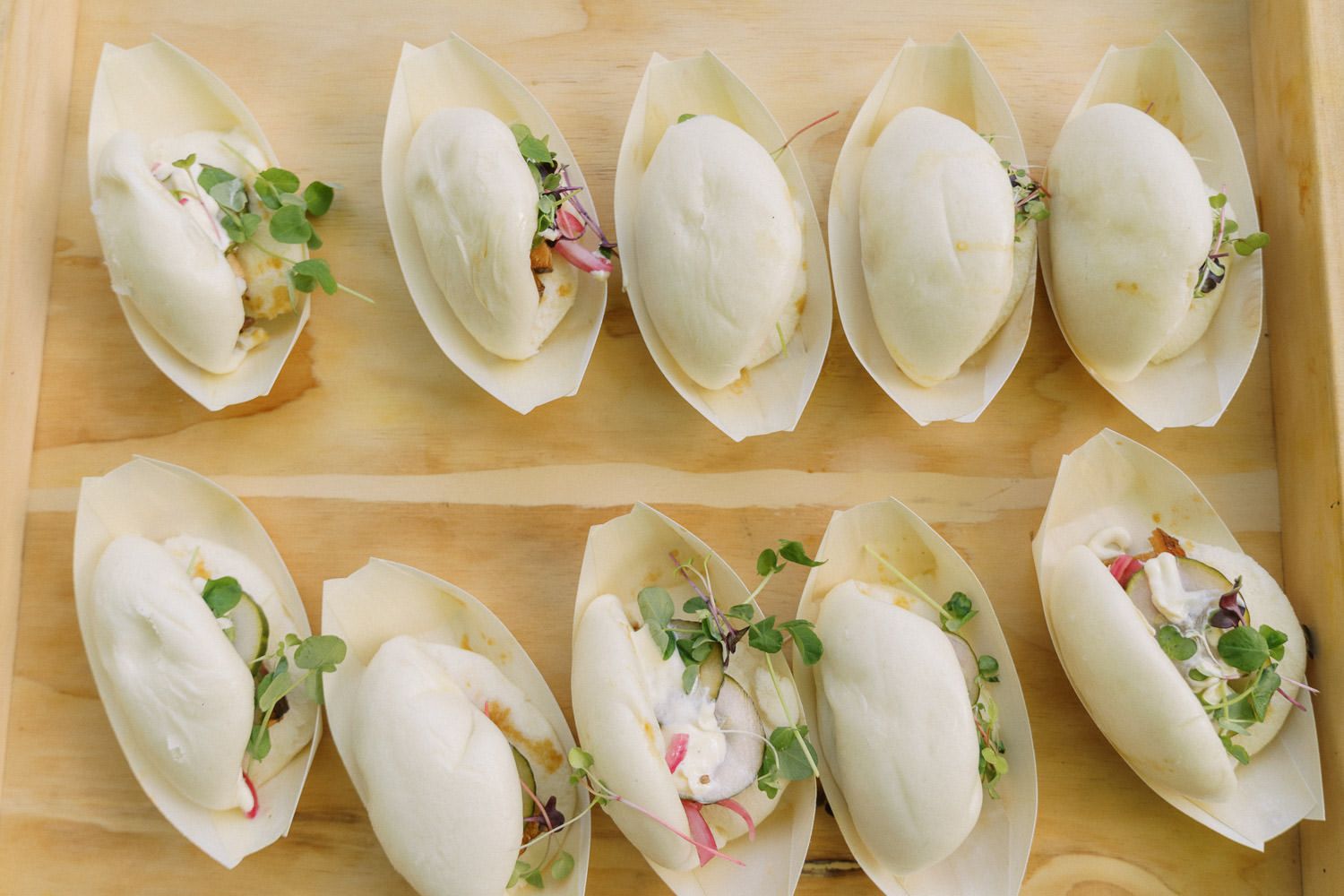 Elegant endive leaf appetizers topped with fresh microgreens and colorful garnishes arranged on a wooden serving tray.