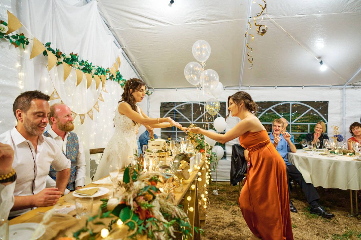 Bride and bridesmaid toast champagne at elegant outdoor wedding reception under white tent with floral decorations.