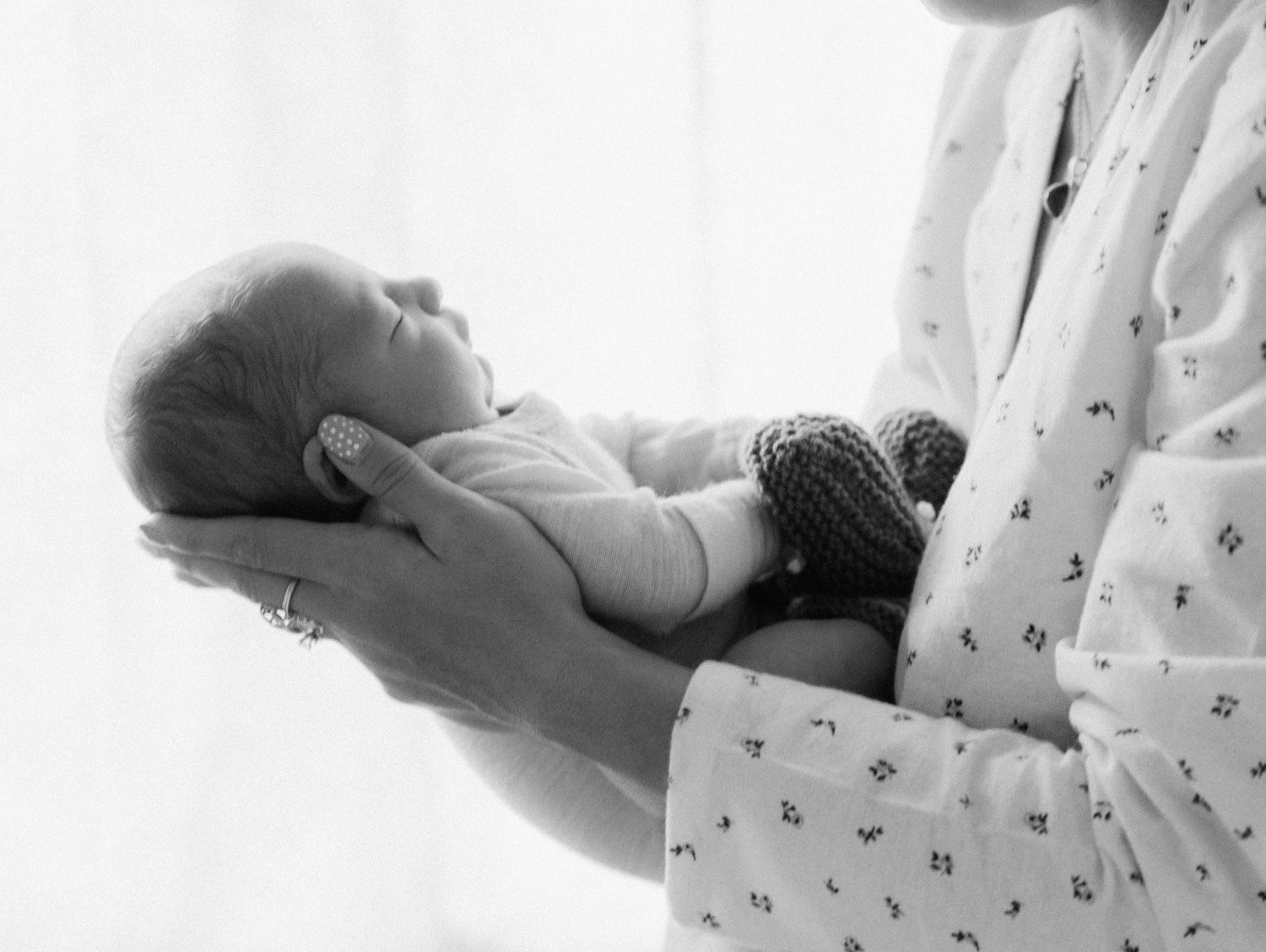 Black and white photo of a newborn baby cradled in an adult's hands, wearing knit booties.
