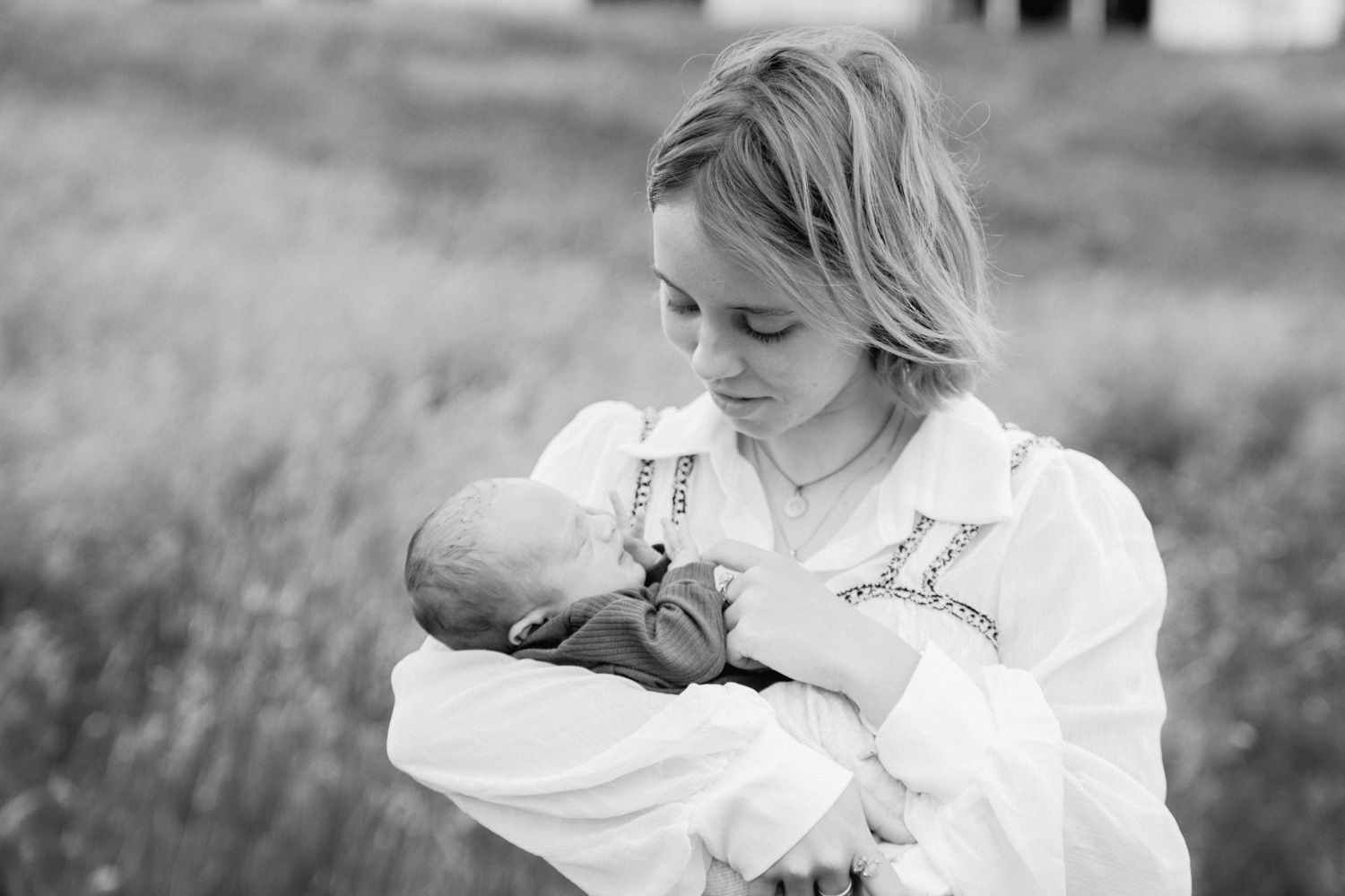 Black and white photo of a young woman tenderly cradling a newborn baby in an outdoor field setting.
