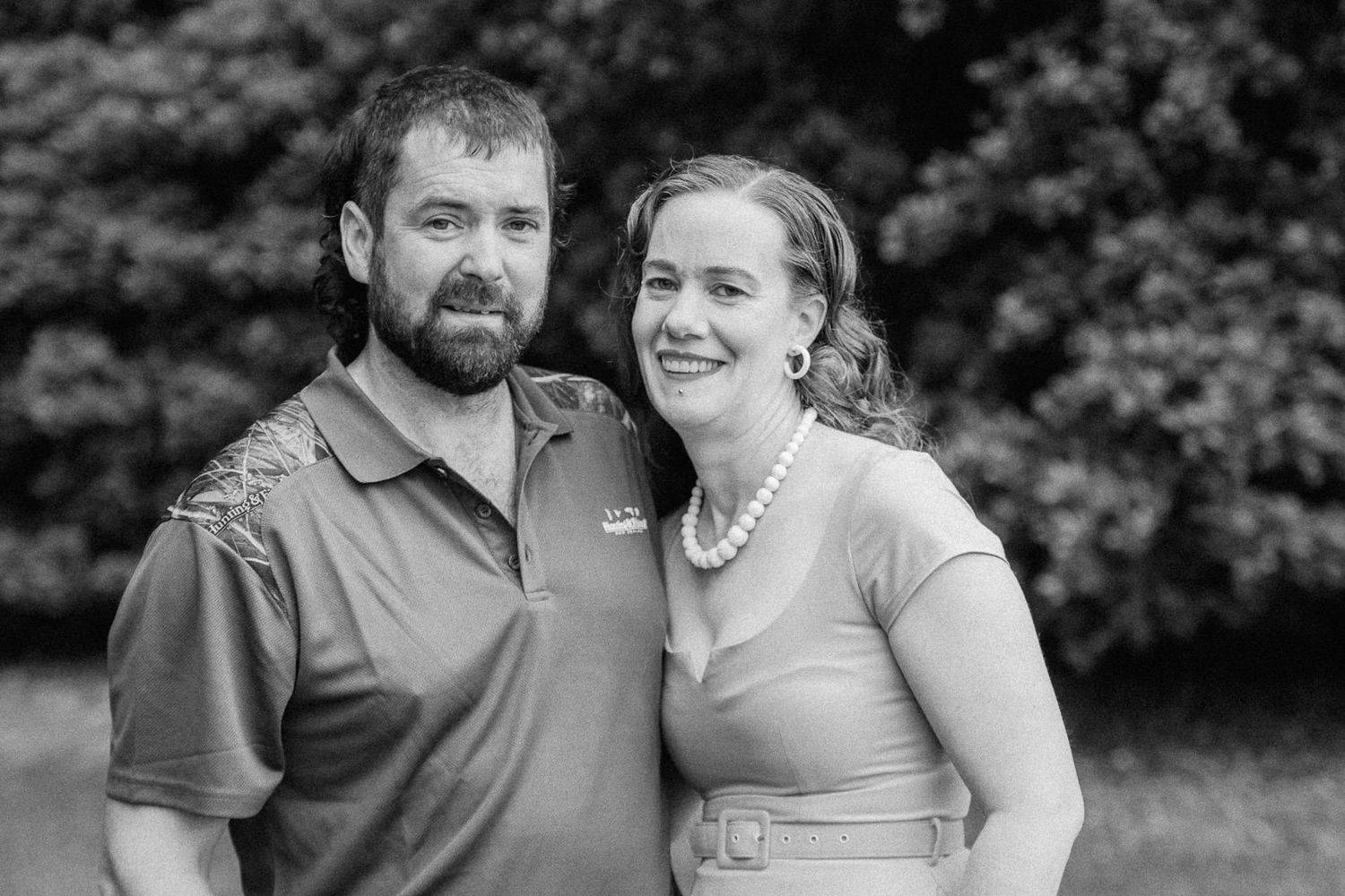Smiling couple poses together outdoors in classic black and white family portrait photography.