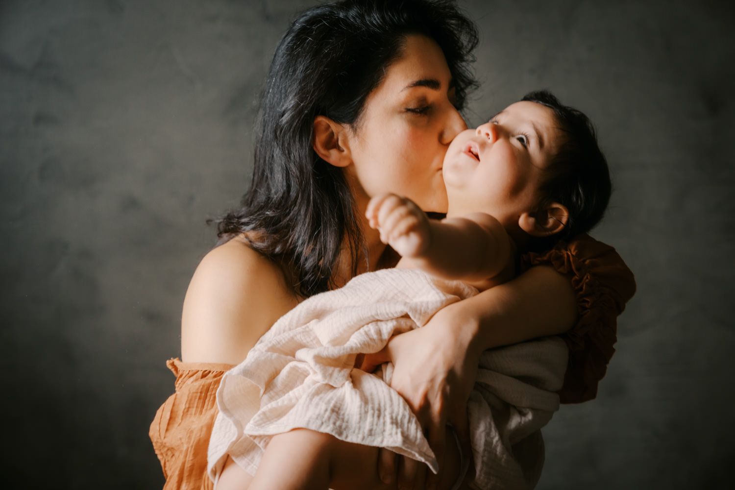 A mother tenderly kisses her baby while gently cradling the infant in her arms.