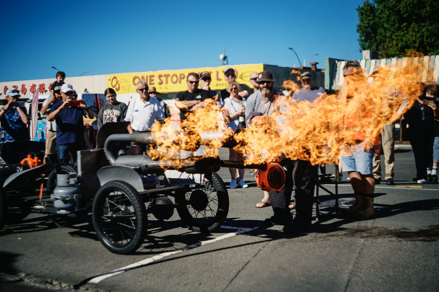 Crowd watches a flame-throwing hot rod car perform a fire show at an outdoor automotive event.